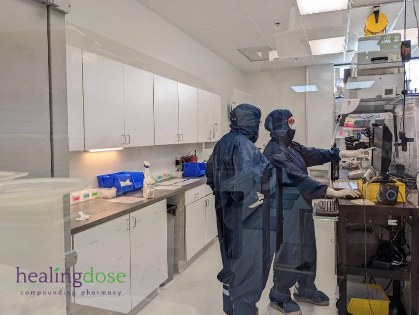 Two laboratory technicians in cleanroom suits operating scientific equipment inside a sterile research lab.